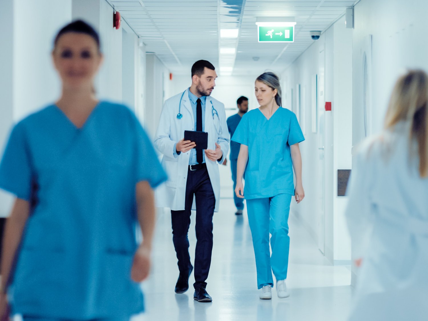 In einem Klinikflur gehen mehrere personen. Zwei Personen reden miteinander.