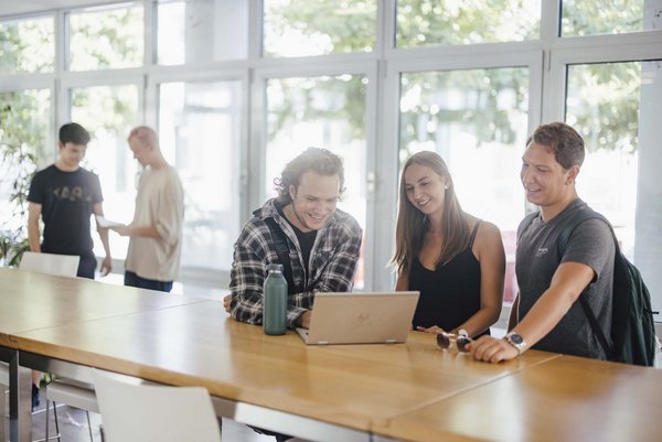 Studierende unterhalten sich an den Hochtischen bei der Cafeteria