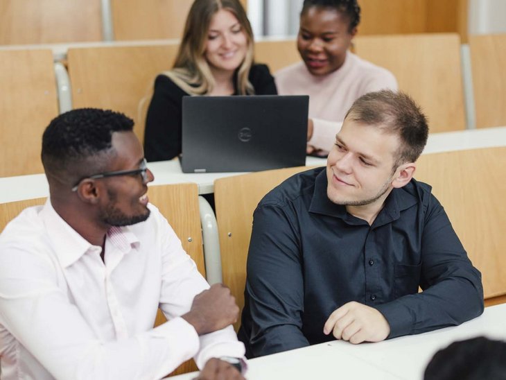 Mehrere Personen sitzen in einen Hörsaal und lächeln sich an.