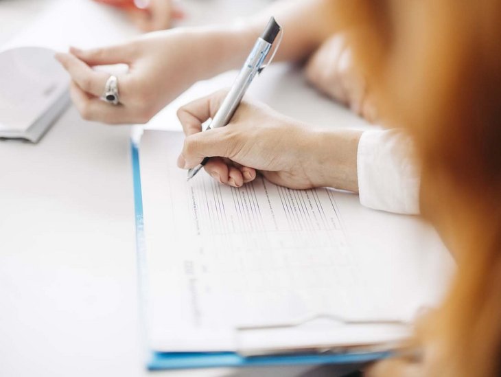 Auf einem Tisch liegt ein Blatt und man sieht eine Hand die einen Stift hält.