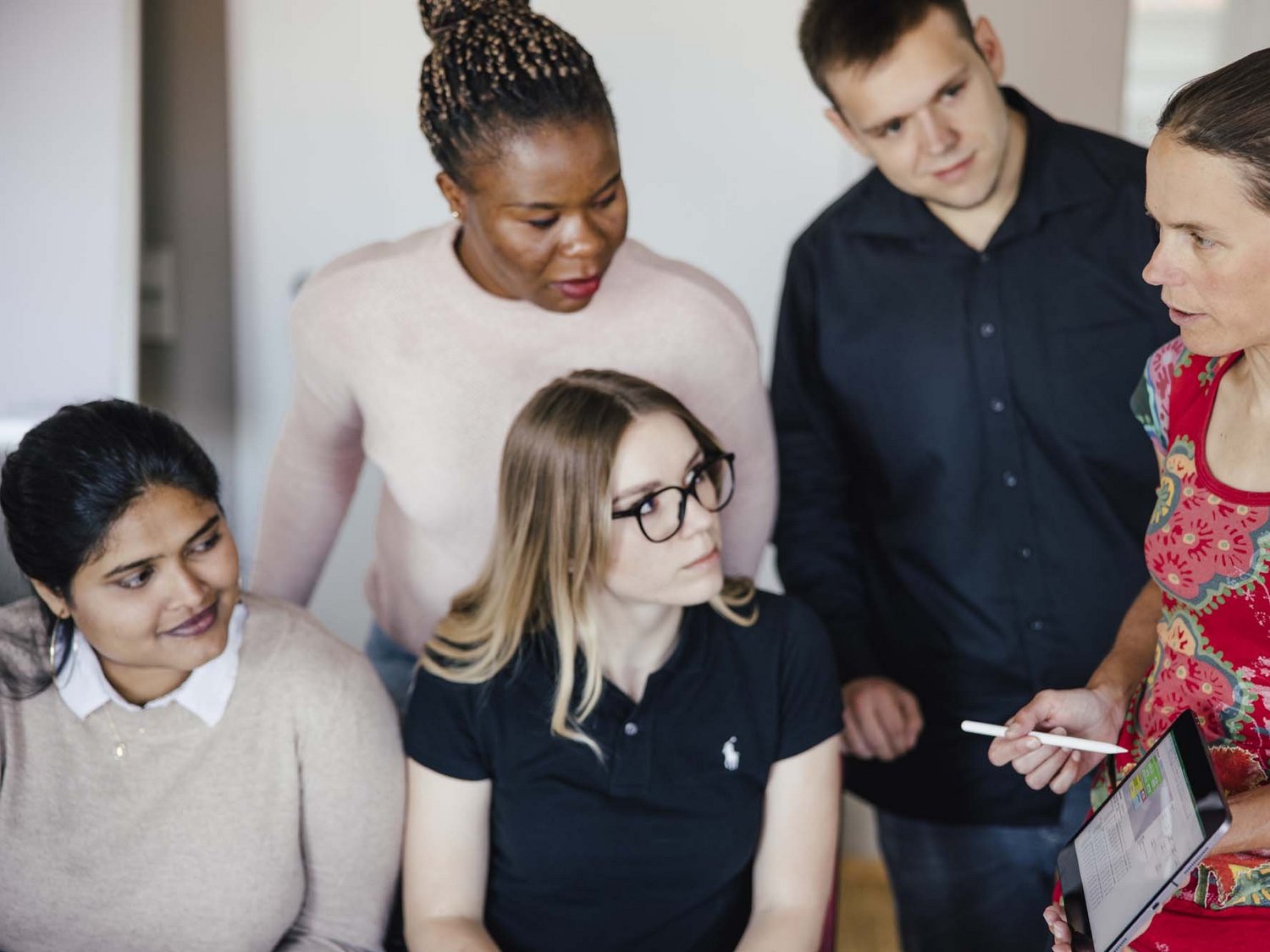 Mehrere Personen sind in einem Raum. Eine Person hält ein Tablet und einen Tablet -Stift in der Hand, die anderen Personen schauen sie an.