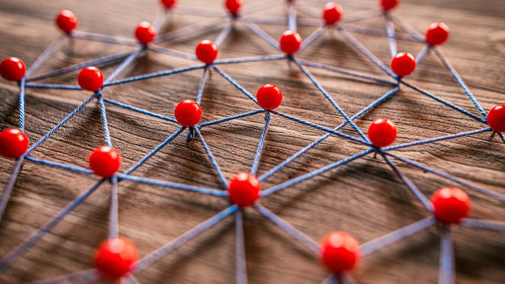 Netzwerk mit vielen Verbindungen mit Stecknadeln und Faden Mehr als 20 Stecknadeln mit roten Köpfen sind in Holz gesteckt. Zwischen ihnen ist blauer Faden gespannt.
