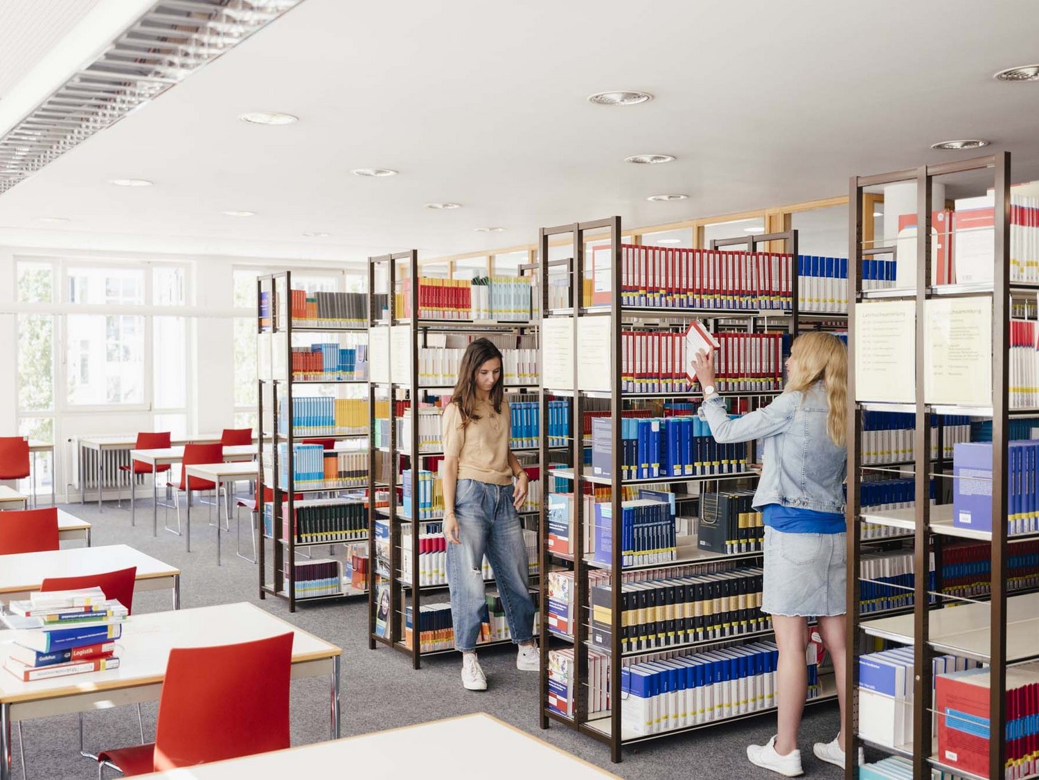 Zwei Personen stehen gegenüber zwischen ihnen eine Bücherwand.